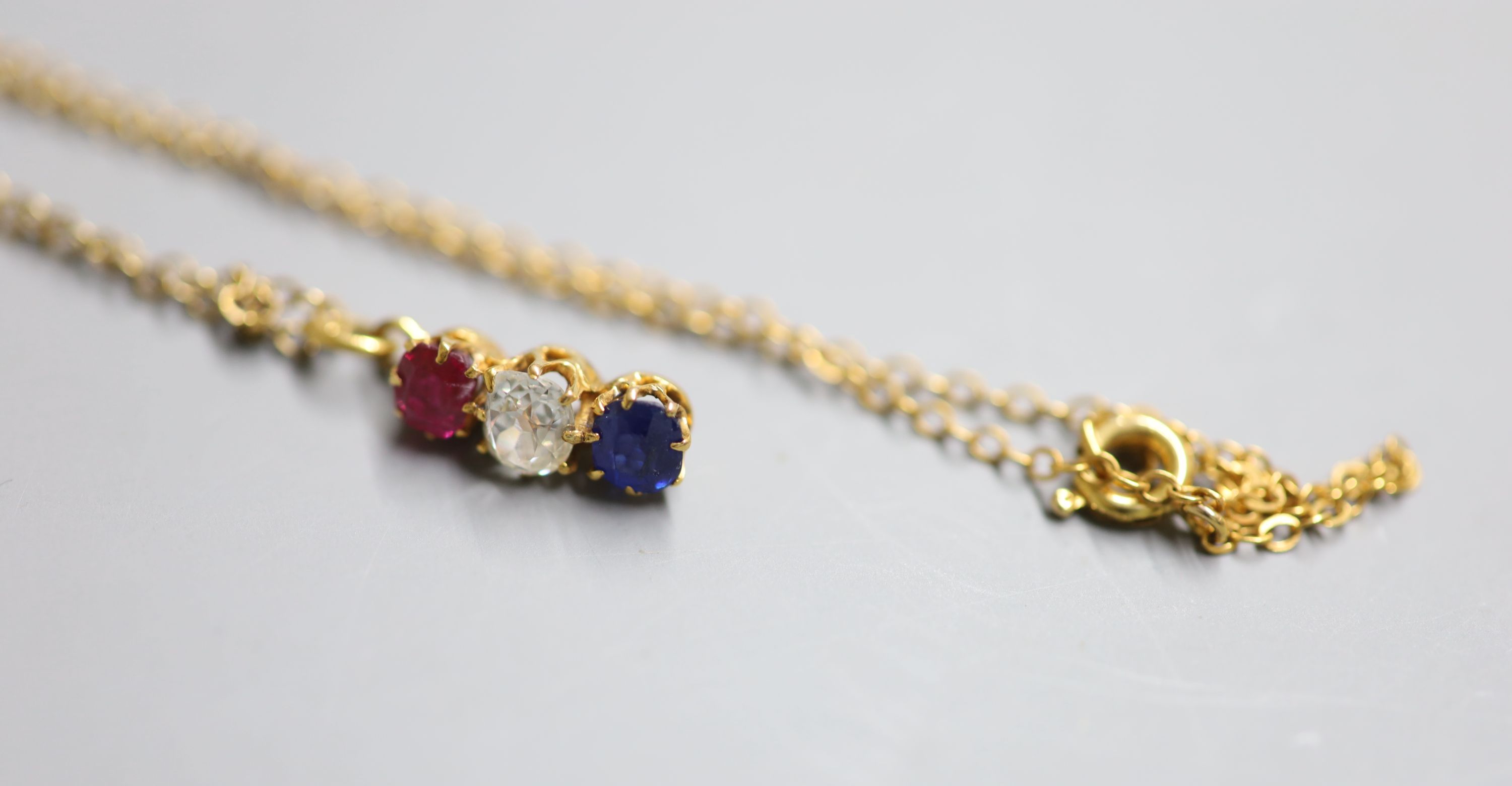 A yellow metal, ruby, diamond and sapphire set line pendant, 14mm, on a yellow metal chain, 38cm, gross 2.4 grams,